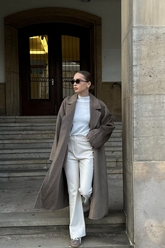 a lady in a white top, a pair of beige pants and a brown long wool coat